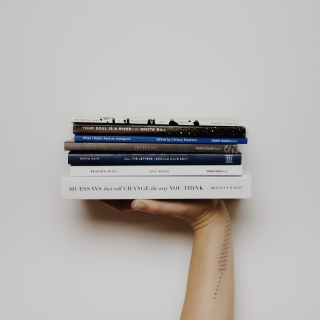 Рука держащая на весу стопку разных книг
